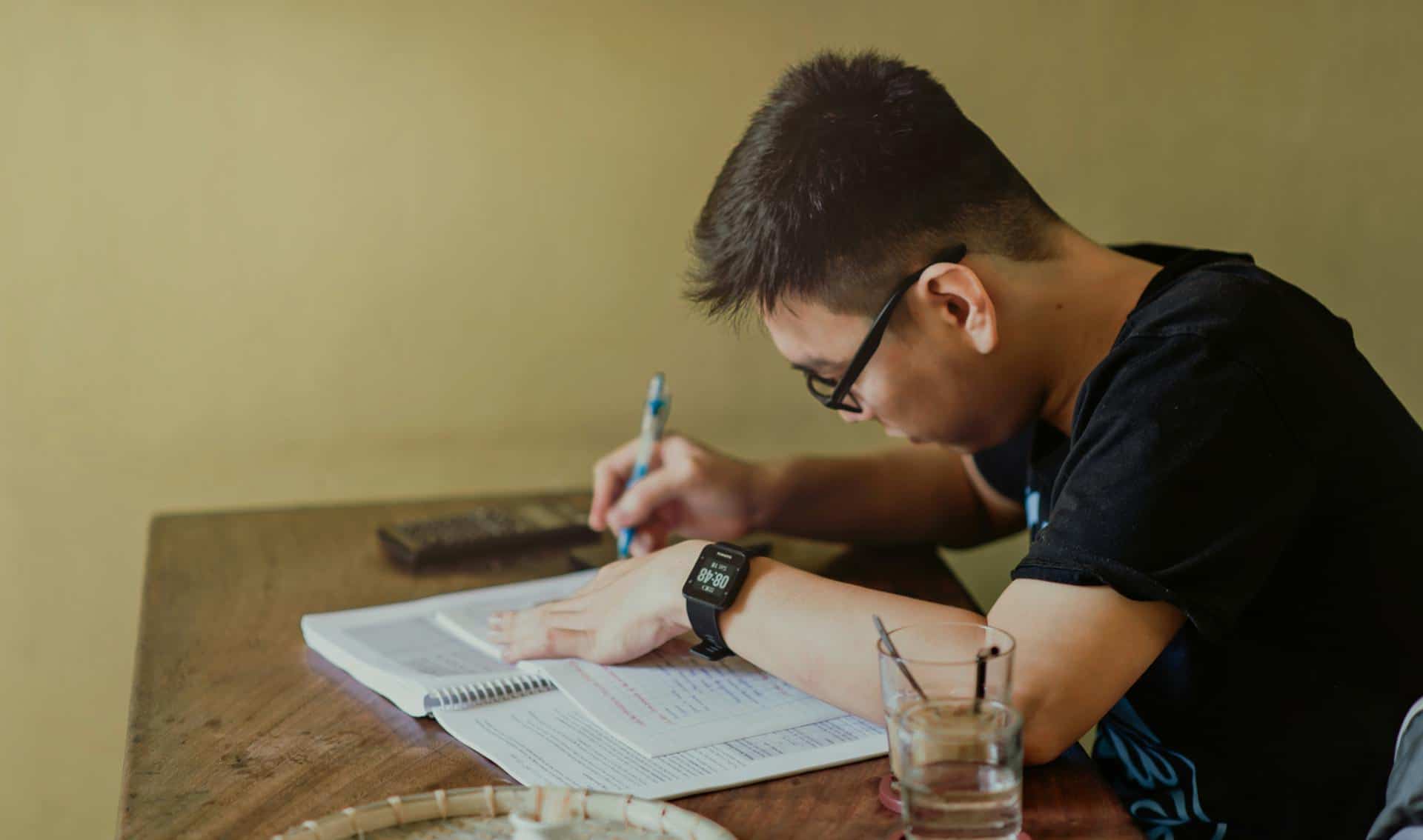 Estudiante estudiando inglés en casa, mejorando vocabulario con recursos digitales y libros en un ambiente cómodo.